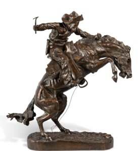 A bronze statue of a cowboy breaking in a wild horse. The horse is rearing up on its hind legs while the cowboy grips onto its mane with one hand while holding a small whip in the other.