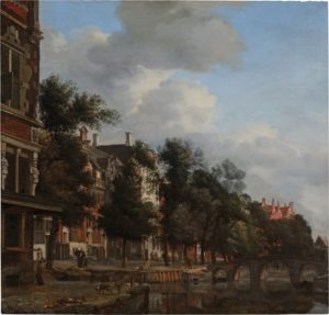 A Dutch street scene of old houses made of wood and stucco beside a series of canals. Trees grow from the ground between the houses and the canals.
