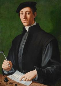 A portrait of a young man against a green background. He is dressed in dark colors, with a grey tunic, a black vest, and a black flat cap. He sits at a desk with a quill in hand, pointing to some lines written in Latin on a sheet of paper.