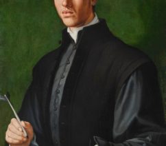 A portrait of a young man against a green background. He is dressed in dark colors, with a grey tunic, a black vest, and a black flat cap. He sits at a desk with a quill in hand, pointing to some lines written in Latin on a sheet of paper.