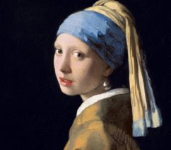 A portrait of a young woman looking towards the viewer over her left shoulder against a black background wearing a blue and yellow turban as well as a pearl earring.