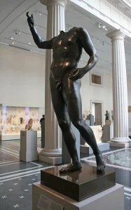 A headless bronze statue in a colonnaded courtyard filled with other antiquities on display at the Metropolitan Museum of Art.