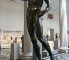 A headless bronze statue in a colonnaded courtyard filled with other antiquities on display.