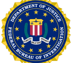 The seal of the Federal Bureau of Investigation, showing a shield with the scales of justice and red and white stripes. This is surrounded by laurel leaves and thirteen stars, with a scroll beneath reading Fidelity, Bravery, Integrity.