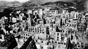 A black-and-white photo of the town of Guernica after its aerial bombing. The hollow shells of buildings are laid out in rows, with no human presence visible.