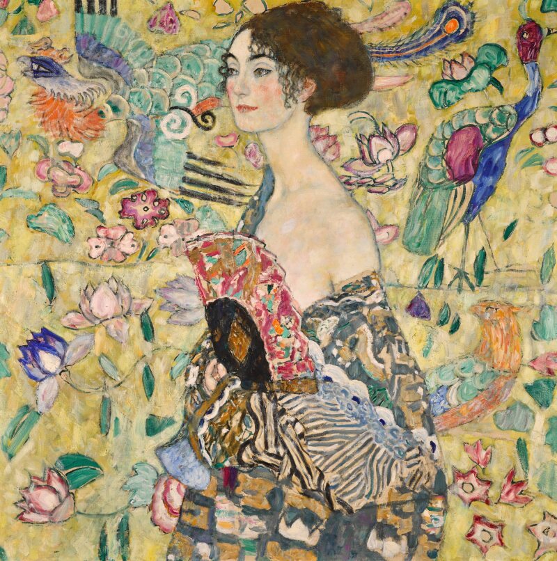 A portrait of a woman in front of an elaborately decorated backdrop. She wears a dressing down slipping off her shoulder, while she hold a fan against her chest.