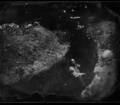 A black-and-white photograph of a soldier sitting on the ground in a trench