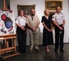 A group of figures, including two police officers, posing in front of five paintings seized as forgeries.