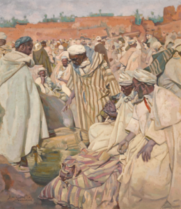 A group of men in white robes and turbans bartering over items in an outdoor market in Morocco.