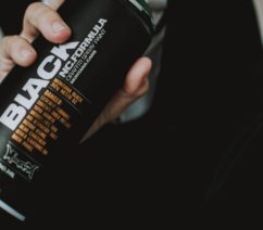 A person in a mask and a black hoodie holding up a can of spray paint in front of their face