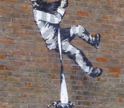 A piece of graffiti showing a prisoner rappelling down a brick wall with a long piece of paper coming from a typewriter.
