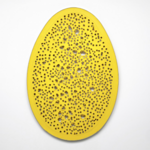An egg-shaped canvas painted yellow with a series of rough holes punctured into it.