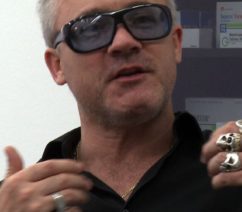 A photograph of the British artist Damien Hirst in a black polo shirt and sunglasses.