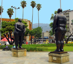 Two bronze sculptures of a large nude man and a large nude woman woman facing one another in a public square.
