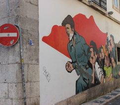 A mural on a street corner showing a group of people rising up against the background of a red flag.