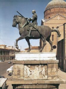 A large bronze Donatello statue of a man on horseback in front of a cathedral in Italy.