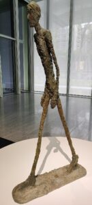 A bronze sculpture of a walking man rendered in a rough, craggy manner