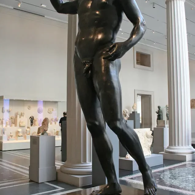 A headless bronze statue in a colonnaded courtyard filled with other antiquities on display.