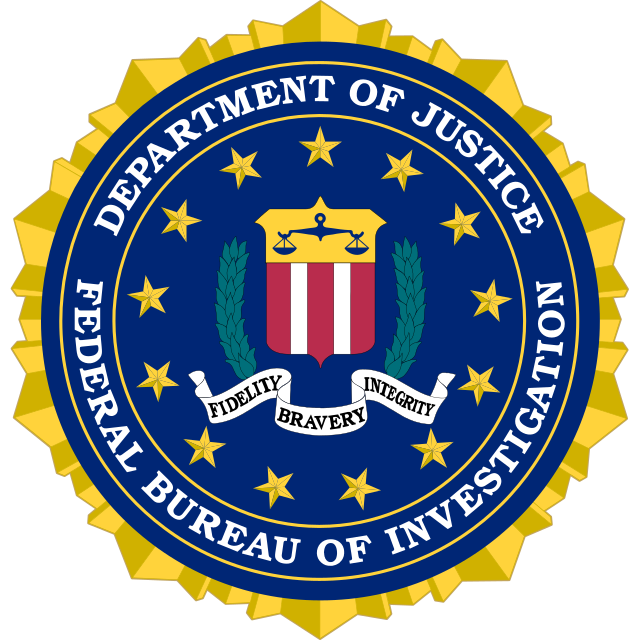 The seal of the Federal Bureau of Investigation, showing a shield with the scales of justice and red and white stripes. This is surrounded by laurel leaves and thirteen stars, with a scroll beneath reading Fidelity, Bravery, Integrity.