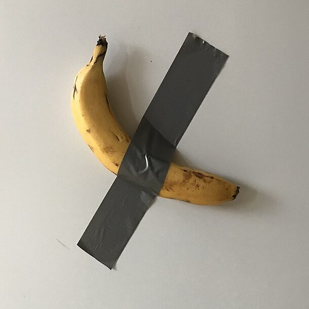 A photograph of a banana adhered to a white wall with silver duct tape.