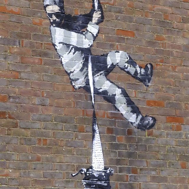 A piece of graffiti showing a prisoner rappelling down a brick wall with a long piece of paper coming from a typewriter.