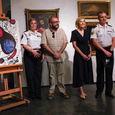 A group of figures, including two police officers, posing in front of five paintings seized as forgeries.