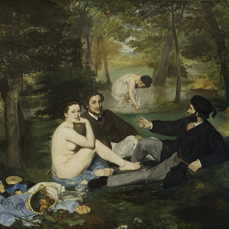A group of figures in a wooded scene near water: two young men are fully dressed reclining on the grass, while the woman next to them is completely nude. Another women in the background is partially dressed while wading in the water behind them. A spread of food including breads and fruit is laid out beside the women's discarded clothes.