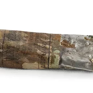 An old, tin paint tube, with the label stained with old paint. The label reads in English, Spanish, and French that it contains emerald green.