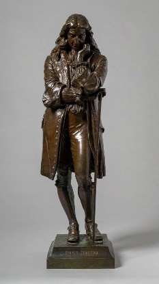 A bronze statue of Edward Colston standing with his hand on his chin.